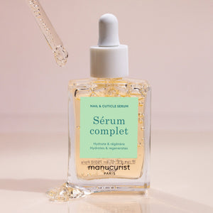 A clear glass dropper bottle labeled “SERUM COMPLET” with light blue and beige accents contains MANICURIST INC’s SERUM COMPLET NAIL HYDRATING SERUM, a transparent formula designed to hydrate and strengthen nails and cuticles.