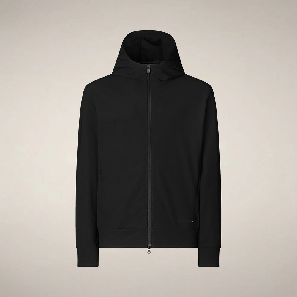 A man faces forward in the SAVE THE DUCK - LUIZ Hooded Jacket in Blue Black from SAVE THE DUCK, paired with black pants and white sneakers, set against a plain beige background.