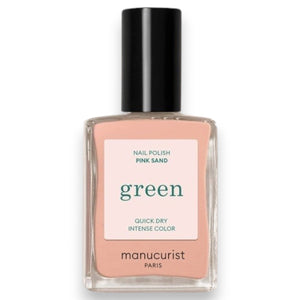 A makeup brush with light bristles sweeps creamy, pink liquid makeup, creating a smooth texture against a matching pink background—perfectly complementing the subtle elegance of MANUCURIST - GREEN™ Nail Polish in Pink Sand by MANUCURIST INC.