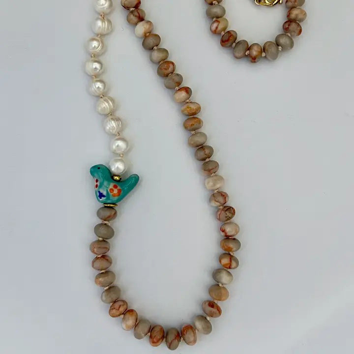The GEMMA NECKLACE by SANDRINE FRANCE STUDIO features alternating freshwater pearls, round Red Vein Jasper beads, a blue ceramic bird bead, and a gold clasp. Handmade in NYC and shown against a plain white background.