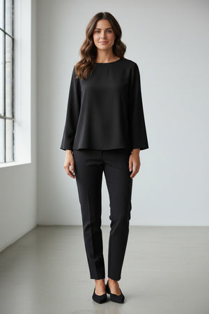 A person wears the MEIMEIJ TOP WITH KNOT BACK DETAIL in bright orange, paired with matching pants, standing against a plain light grey background. Their face is partially out of frame.