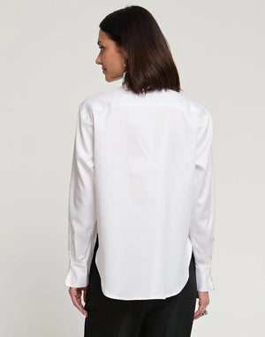 A person with short, brown hair is standing and facing away from the camera, wearing a HINSON WU - HALSEY LONG SLEEVE COTTON SATIN SHIRT WITH FLOWER. They have paired this black button-up shirt, made of a cotton and spandex blend, with light-colored pants. The background is plain and light-colored.