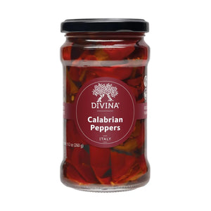 A blue bowl filled with vibrant red DIVINA - CALABRIAN PEPPERS, their stems still attached, sits on a beige cloth with dark stripes atop a wooden surface.