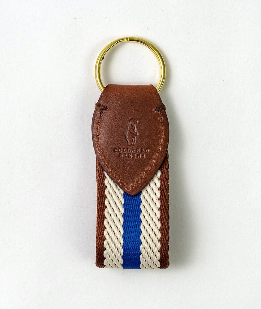 The COLLARED GREENS Dockside Key Chain by Bird Dog Bay features a gold ring, brown leather embossed with a golfer and "COLLIER GREENS," plus a navy and white striped woven strap. Proudly American made.
