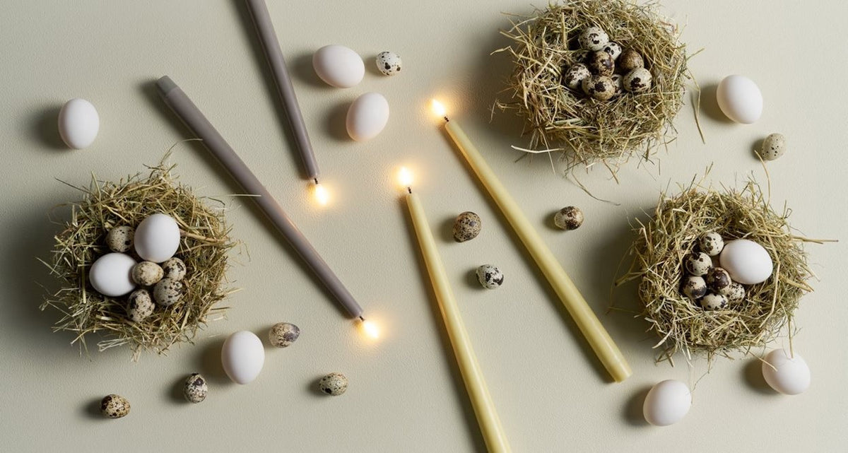 Two PIFFANY UYUNI Ivory Slim Taper Candles (1x12.6) with small yellow flames stand upright side by side against a plain white background, exuding timeless elegance.