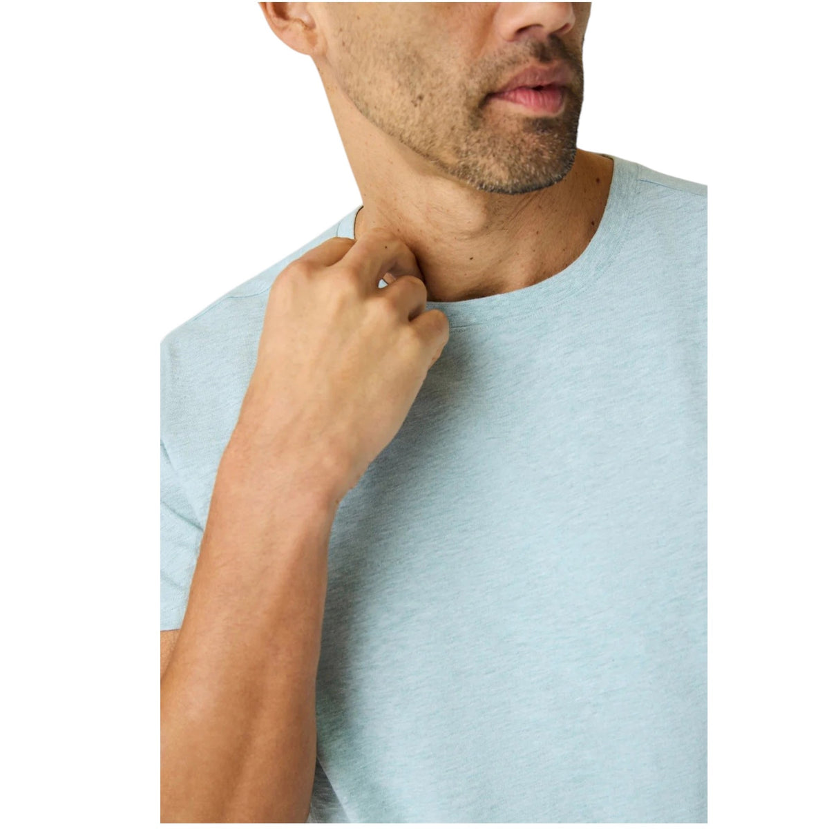 A man with short hair stands with his back to the camera, wearing the MACK WELDON Slub Cotton Crew Neck T-Shirt in Nile Blue Heather and dark pants. His hands are in his pockets as he glances over his left shoulder.