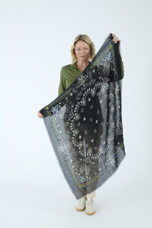 The STORIATIPIC - NELLY Wool Bandana Scarf with Embroidery in Black features a sophisticated paisley and floral design in shades of blue, green, and white. Delicately finished with small frayed edges and shown folded in a loose loop against a white background, this elegant accessory captures the essence of French designer flair, expertly crafted by STORIATIPIC to elevate any ensemble.