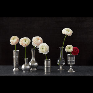 The MATCH Footed Cylinder Pewter Vase by MATCH displays a bouquet of pink, peach, and yellow ranunculus against a white background—an elegant and timeless hostess gift.