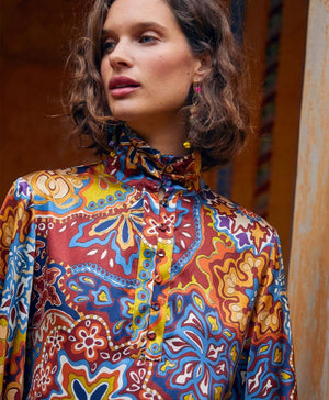 The MOMONI - THIERRY BLOUSE IN PRINTED STRETCH SATIN is a long-sleeved, oversize silk blouse with a multicolored paisley and floral print, high pleated collar, and buttoned cuffs, shown on a plain white background.