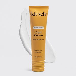 A woman with curly hair smiles and holds a yellow tube of KITSCH - MOISTURIZING CURL CREAM near her face against a neutral background, highlighting her smooth, defined curls achieved with this effective KITSCH frizz control product.