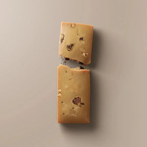 A gold protein bar wrapper labeled “STARS+HONEY” featuring the flavor “Cacao Salt Caramel Peanut” is placed on a beige background, highlighting 10g collagen, 15g protein, and just 2g sugar as a low sugar protein bar option.