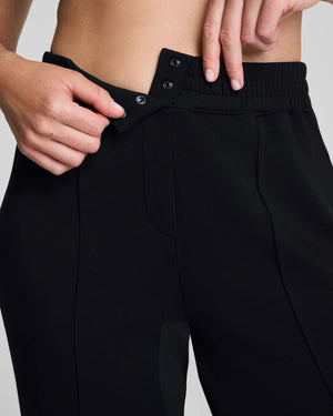 A person models the SPANX - AIRessentials Brushed Slim Straight Pant with an elastic waistband and buttons, paired with black slip-on shoes against a plain light background.