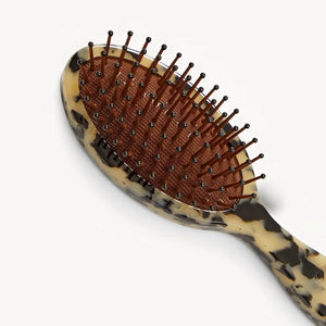 The MACHETE Petite Travel Detangling Hair Brush in Blonde Tortoise features nylon bristles on a brown cushioned pad and a marbled beige-and-black Italian acetate handle—ideal as a compact travel brush.