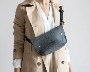 The WOOLBERRY - FELTED WOOL BELT BAG by WOOLBERRY is a small green belt bag crafted from felted wool, featuring a flap secured by two silver snap buttons, and is displayed against a white background.