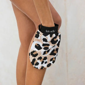 The KITSCH Eco-Friendly Exfoliating Glove boasts a leopard print with black spots on a beige and white background, designed perfectly for bath or shower scrubbing. It features a convenient black tag with white text at the top.