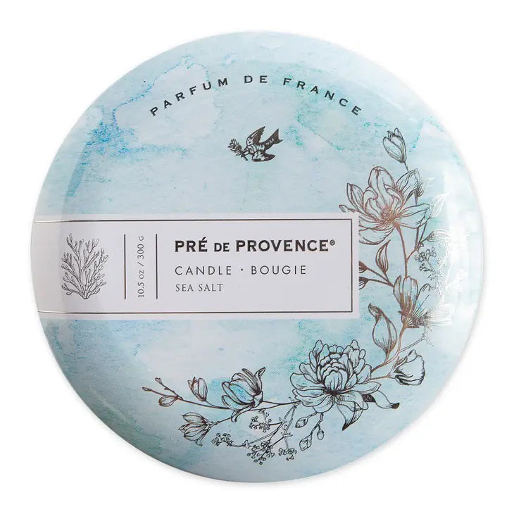 The 3 Wick Candle - Sea Salt by European Soaps, LLC comes in a round tin adorned with a pale blue watercolor design featuring floral and botanical illustrations. The text reads &quot;Parfum de France, Pré de Provence, Candle Bougie, Sea Salt, 10.5 oz/300g,&quot; and the design includes an illustration of a bird at the top. This candle is ideal for enhancing home ambience with its sparkling aldehydes scent.