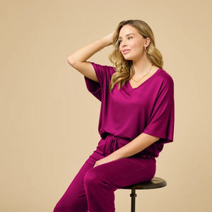 A woman wears a SOFTIES - DREAM RELAXED V-NECK WITH CAPRI LOUNGE SET in magenta, featuring a V-neck top with elbow-length sleeves and matching cropped drawstring pants, paired with cream-colored loafers.