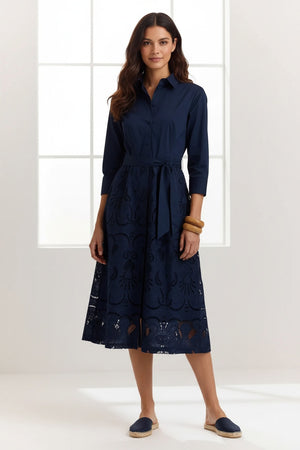 A woman stands against a plain light background wearing the HINSON WU Robin 3/4 Sleeve Eyelet Embroidery Dress in navy, featuring a collared neckline, belted waist, and an elegantly detailed lace-patterned skirt.