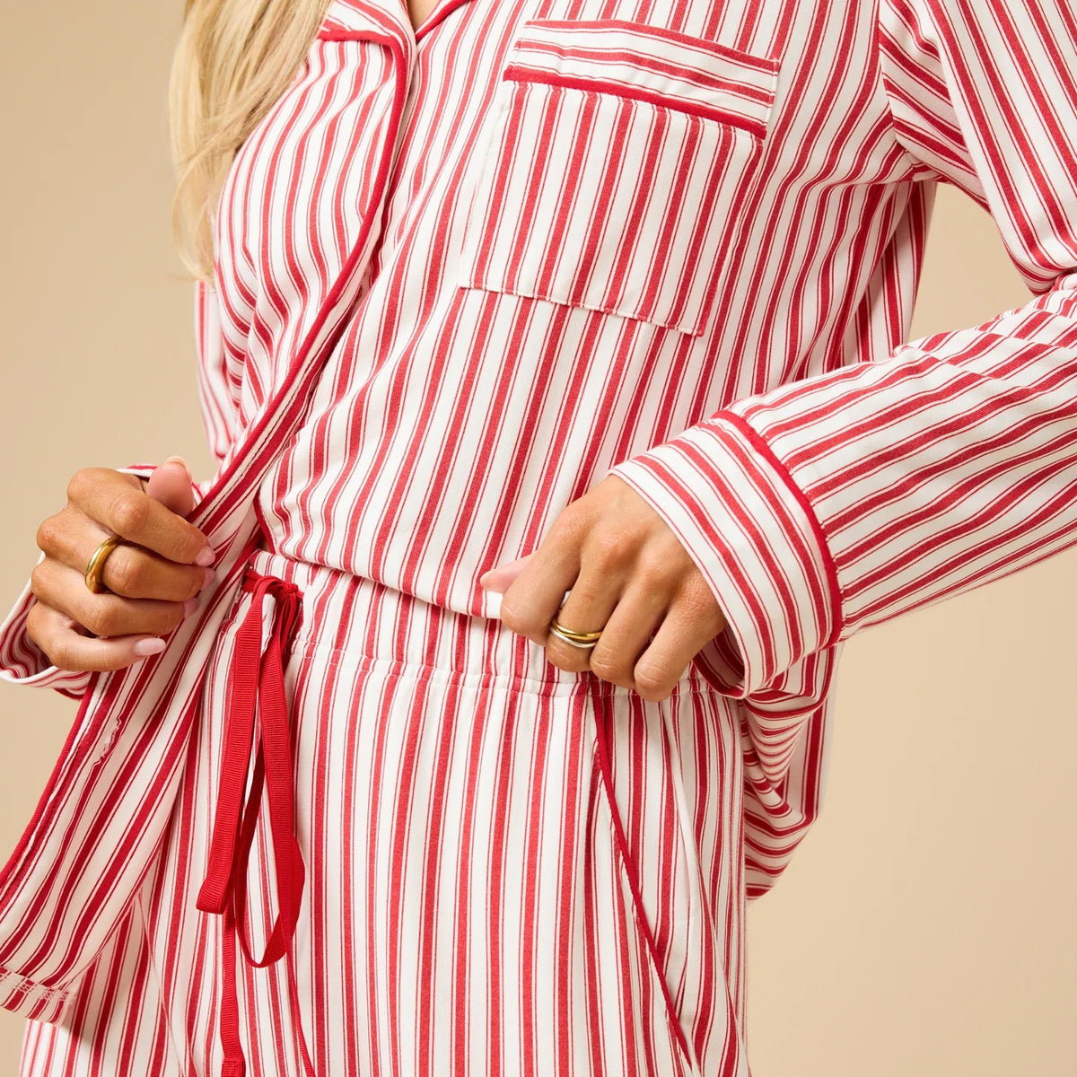 A woman wears the SOFTIES ARIA SLIM NOTCH COLLAR PJ SET, featuring a long-sleeved button-down top and matching wide-leg pants in red and white vertical stripes with red piping details.