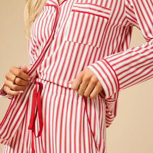 A woman wears the SOFTIES ARIA SLIM NOTCH COLLAR PJ SET, featuring a long-sleeved button-down top and matching wide-leg pants in red and white vertical stripes with red piping details.