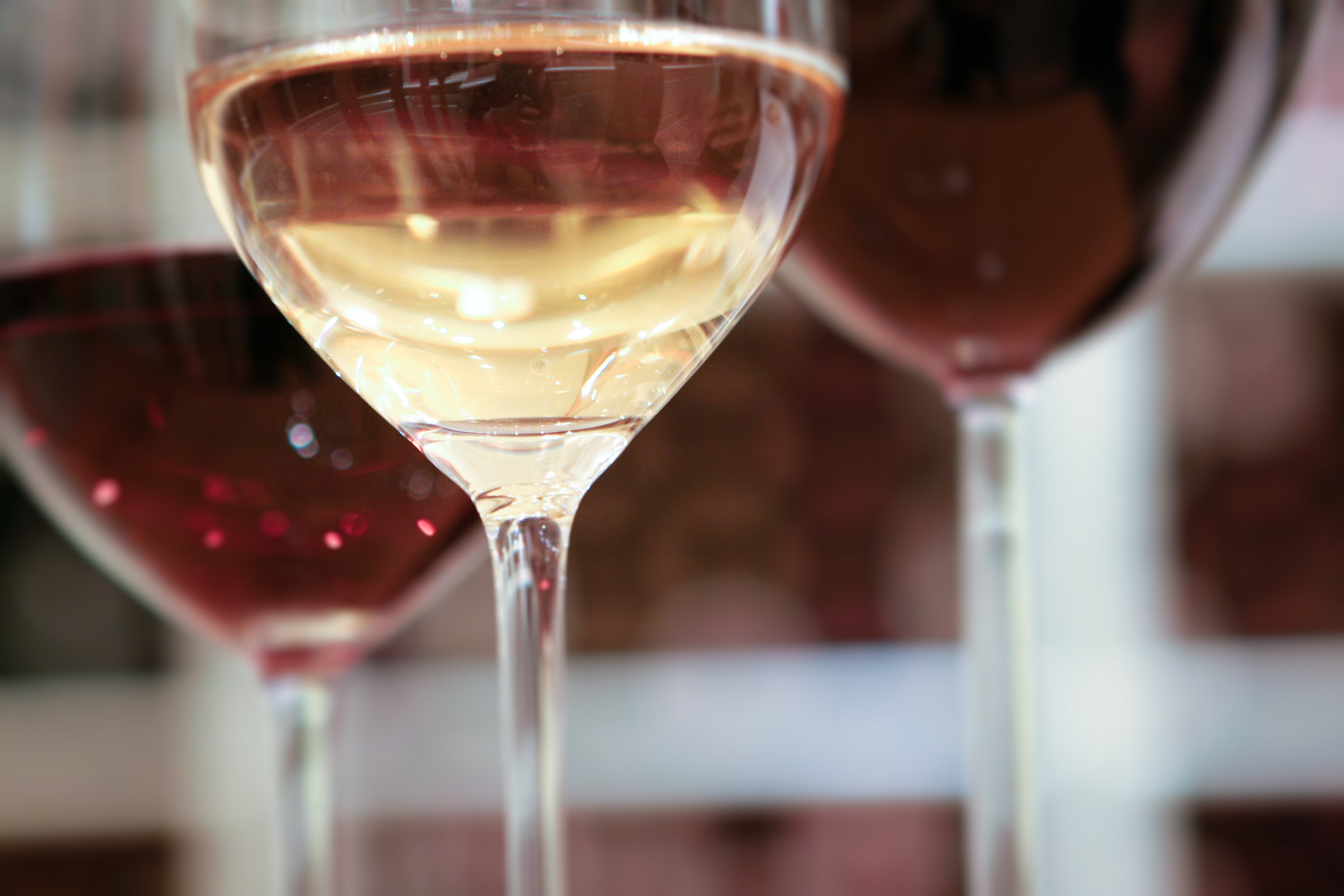 Three wine glasses close up: one filled with white wine in the center, and two with red wine on either side, with a blurred background.
