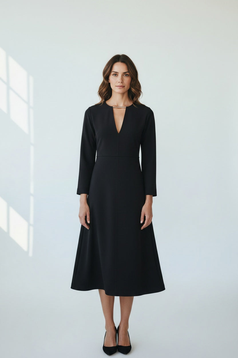A model wears the MEIMEIJ Long Sleeve Dress with Metallic Collar—a black, midi-length dress with a V-neckline by MEIMEIJ—standing against a textured light background.