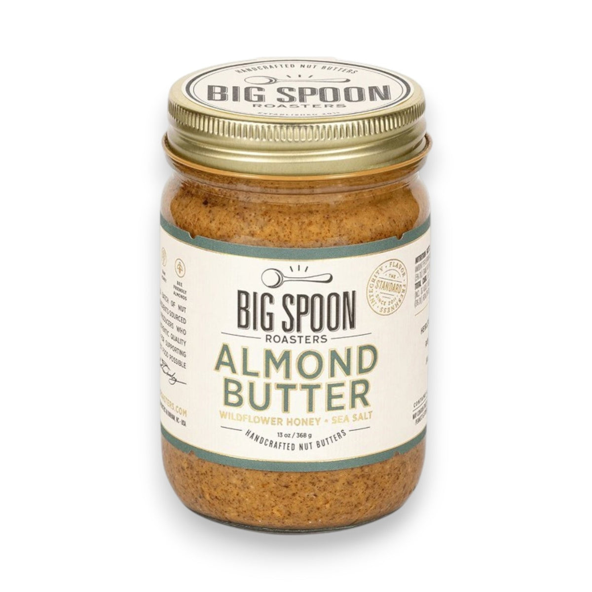 A glass jar of BIG SPOON ROASTERS - ALMOND BUTTER WILDFLOWER HONEY NUT BUTTER with a gold lid and a white label featuring branding and product details in black and gold text.