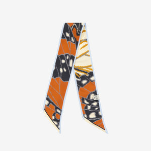 The INOUI EDITIONS - PAPILLON (BUTTERFLIES) SILK RIBBON by INOUI features a butterfly wing print in orange, black, white, and yellow—an elegant silk scarf to elevate any outfit. Displayed on a white background.