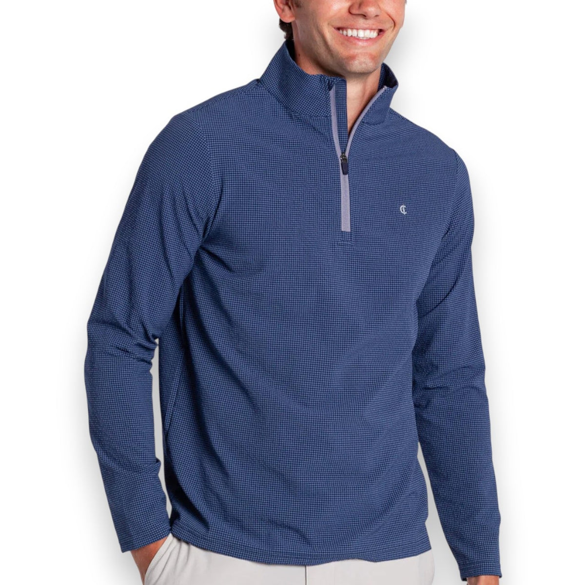 A man in the CRIQUET Seersucker Performance Pullover in Navy and light pants smiles with his hand by his side; this lightweight layer from CRIQUET offers UPF 50 protection against a simple background.