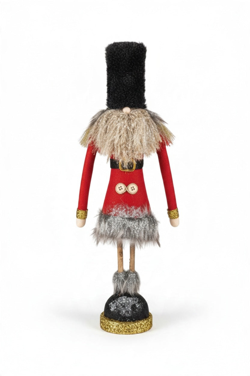 SOLDIER WITH GLITTER AND TWIG LEGS whimsical fabric figurine with a tall black hat, red coat, two buttons, and twig legs standing on a glittery gold and black base.