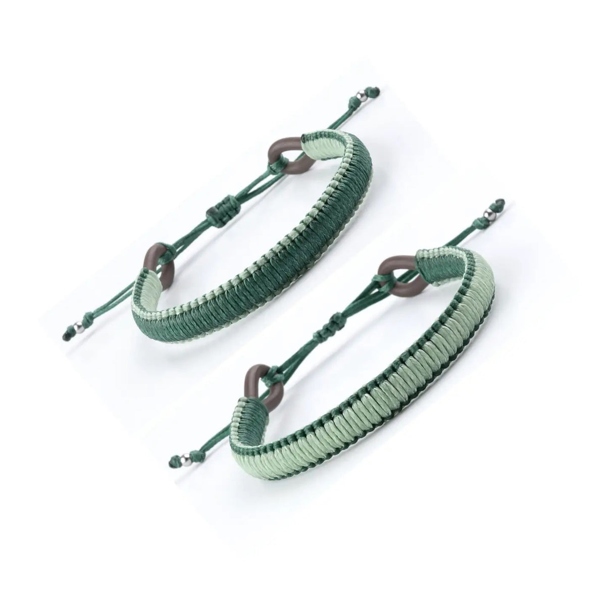 A close-up of a person's wrist wearing the MAKARLA MEN'S REVERSIBLE SURFER BRACELET in mint/hunter green. The person is dressed in a green shirt and blue jeans with a small tear near the pocket.