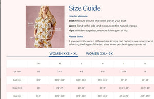 A woman stands barefoot indoors against a white paneled wall, gazing at the camera with a relaxed expression while wearing the PRINTFRESH - BAGHEERA ECO SATIN CHIC TO SLEEP NIGHTIE IN INK by PRINTFRESH, a spaghetti strap maxi nightie crafted from eco-friendly viscose satin and featuring a cheetah and foliage Bagheera print.