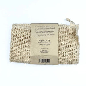 The BAUDELAIRE - SISAL WASH CLOTH by BAUDELAIRE is crafted from natural sisal fiber, harvested by hand, and features a woven texture with a brown paper label that reads “Baudelaire Sisal Wash Cloth, natural sisal fiber, harvested by hand.” This gentle exfoliator is ideal for daily cleansing or as a facial scrub, offering the benefits of natural sisal to your skincare routine.