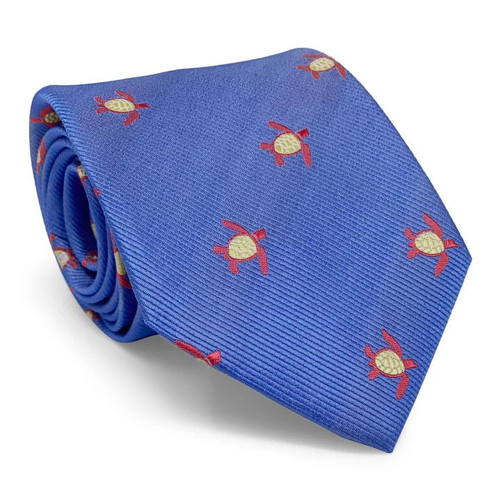 The BIRD DOG BAY PETER-BLAIR - TURTLES SILK TIE IN BLUE is a handmade woven silk tie with a repeating red and yellow sea turtle pattern, crafted in New York.