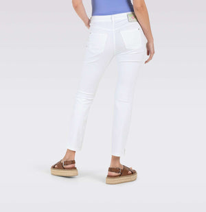 With long brown hair, a person stands against a plain backdrop wearing MAC's tan cropped jacket and MAC JEANS - DREAM SUMMER light blue slim jeans made from a comfortable modal blend. White heels complete the look as they gaze ahead with relaxed arms by their sides.