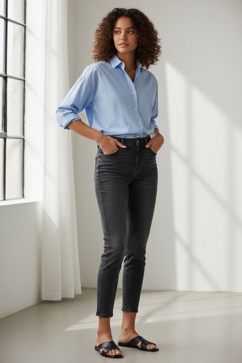 A woman strolls on a brick path under a vine-covered archway, wearing sandals, a white button-down shirt, and FRANK &amp; EILEEN's SLIGO SKINNY JEAN IN 1991 WASH with a high-rise contour waistband for comfort.