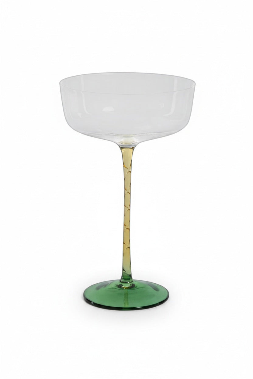Four VICENZA GREEN AND AMBER COCKTAIL/MARTINI GLASS 325 ml soda-lime drinking glasses with amber stems and green bases on a metal tray, accompanied by two glass spheres with amber and green accents.