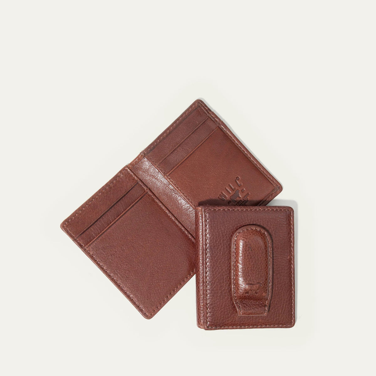 The WILL LEATHER GOODS Classic Money Clip sits atop an open full-grain leather wallet, both in brown, showcasing card slots against a plain light background.