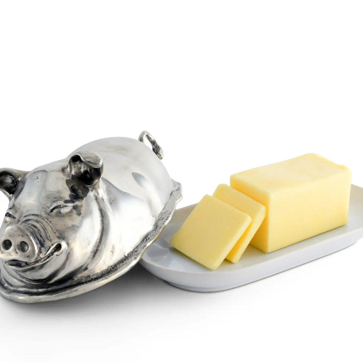The VAGABOND HOUSE Pewter Happy Pig Butter Dish, a luxury-grade piece by VAGABOND HOUSE, gleams beside a white plate with butter and two slices, its lid open against a pristine white backdrop.