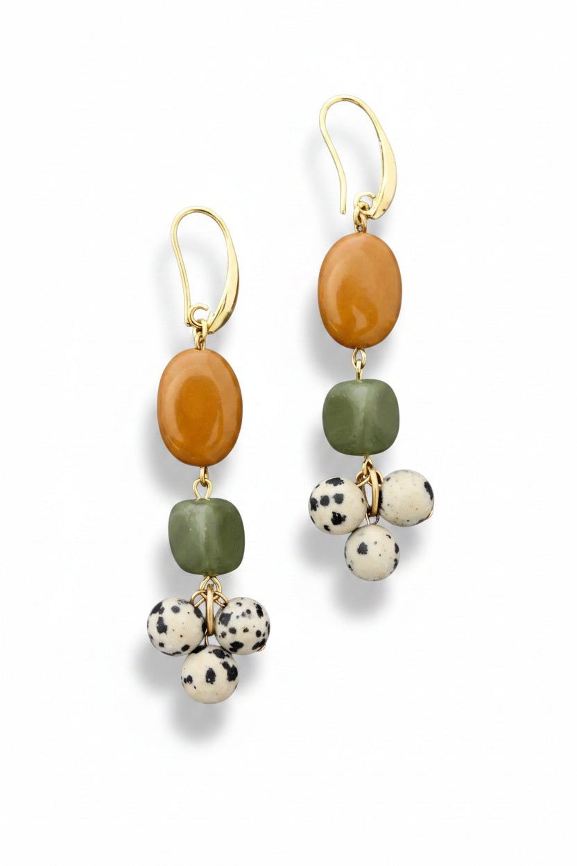 DAVID AUBREY JASPER SERPENTINE DALMATION CLUSTER EARRINGS by DAVID AUBREY feature gold-plated brass, an oval amber bead, a square green bead, and three small Dalmatian-spotted white beads against a gray background.
