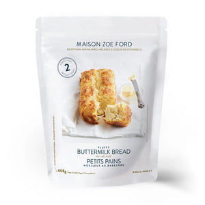 A white package of MAISON ZOE FORD - FLUFFY BUTTERMILK BREAD mix is shown. The front features an image of buttery buttermilk bread on a white plate with an open jar of honey and a honey dipper. The 608-gram package makes 8 fresh dinner rolls.