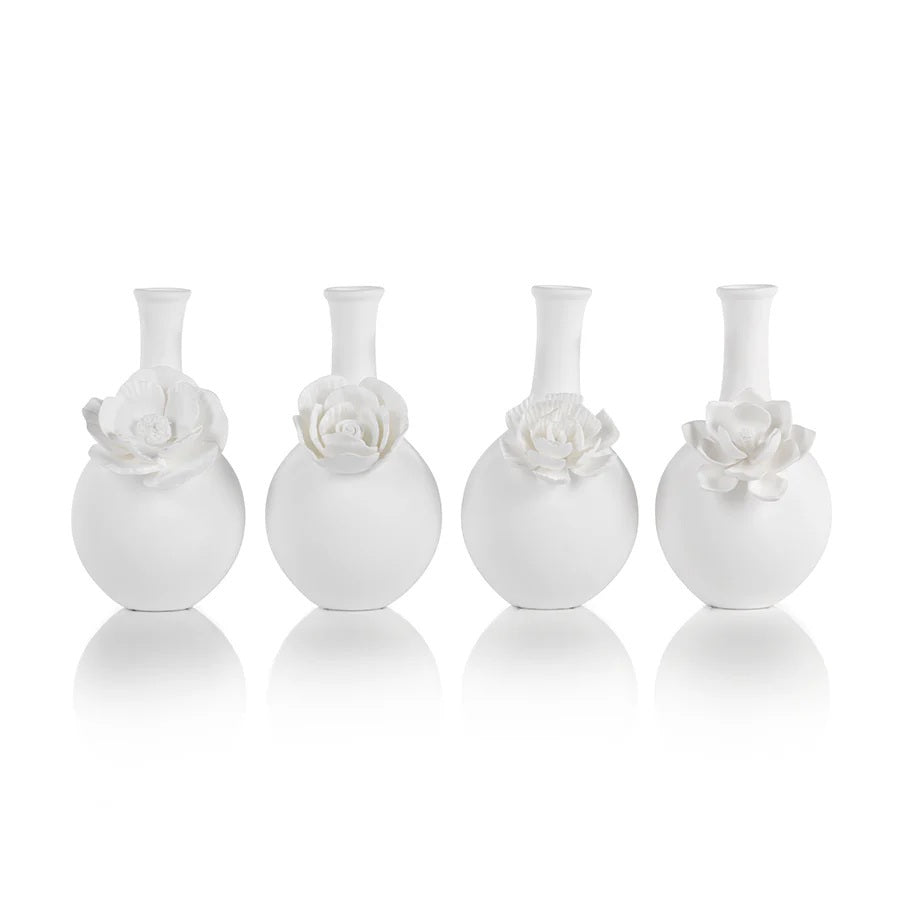 The CAMEO LONG NECK PORCELAIN BUD VASE by ZODAX is a round, white vase with a matte finish, featuring a narrow neck and a detailed floral embellishment on the front.