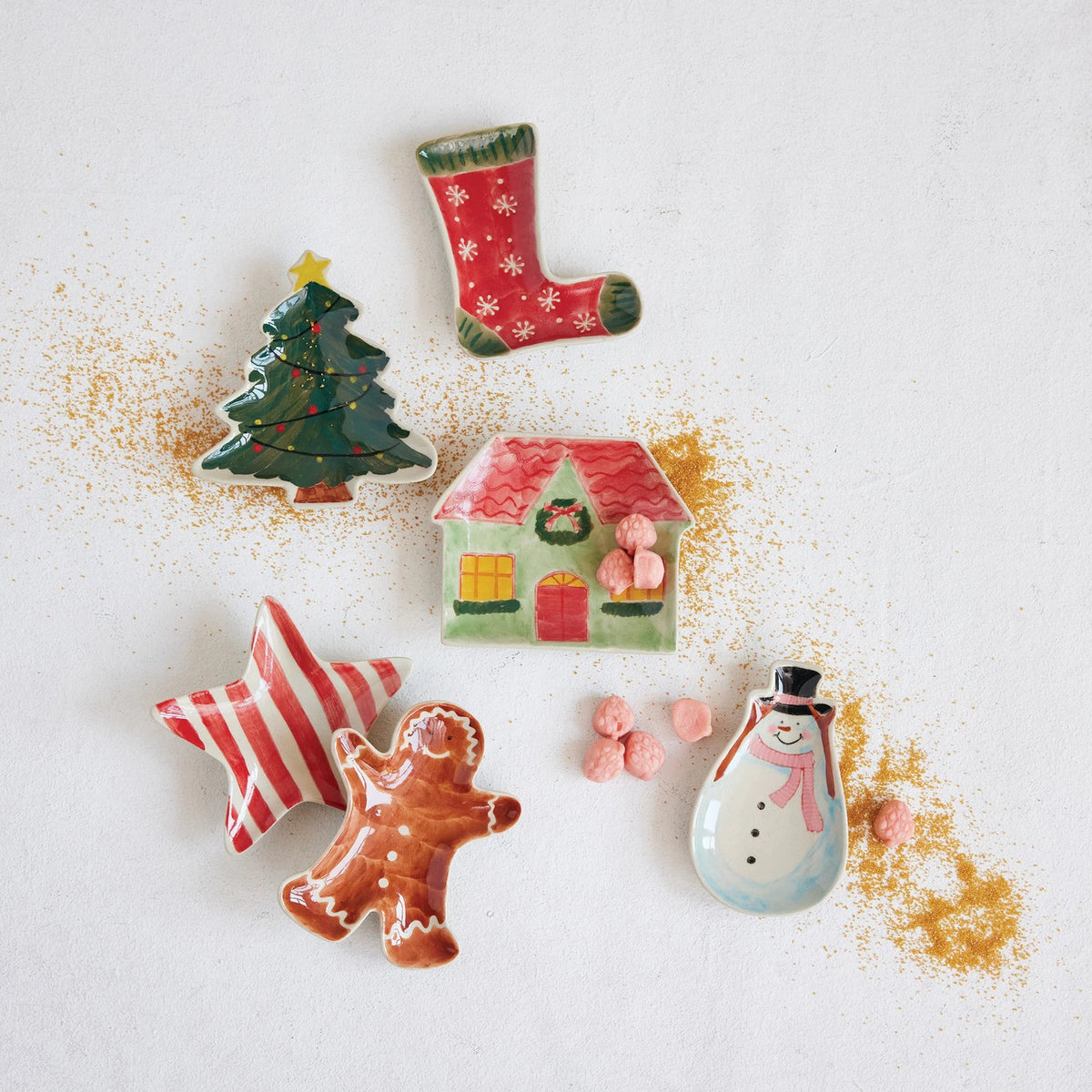 CREATIVE COOP HAND PAINTED HOLIDAY SHAPED DISHES—stocking, tree, and star designs—are displayed on a white background with golden sprinkles and pink candies for a festive look.