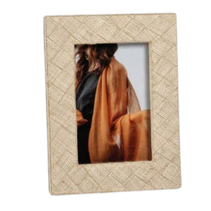 Showcasing the LA BOCCA WOVEN RAFFIA FRAME - 4X6 by ZODAX, this decorative beige frame features a textured woven raffia pattern and displays a portrait of a person draped in a sheer orange-brown shawl over a black outfit, partially turned away from the camera—perfect for introducing an organic touch of home decor to any space.