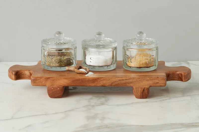 The ETUHOME Bistro Glass Salt Cellar with Scoop sits on a wooden tray atop a marble counter, accompanied by two other glass jars for herbs and sugar. A small wooden scoop from ETUHOME rests in front.