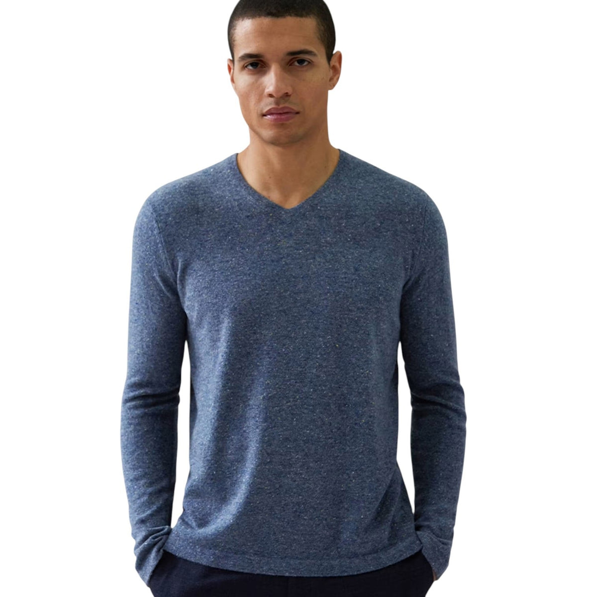 A man stands against a white background, wearing the AUTUMN CASHMERE Basic V Neck with Open Bottom in Oxford—a high-quality blue cashmere sweater from AUTUMN CASHMERE—with his hands in his pockets.