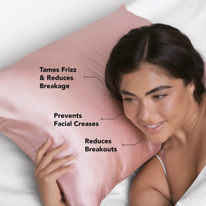A silky KITSCH satin pillowcase in light pink is elegantly displayed against a plain backdrop, symbolizing luxury. A matching KITSCH frizz-free satin scrunchie is draped over it, while a box labeled "600 Thread Count" sits beside the pillow containing another beautiful satin pillowcase.