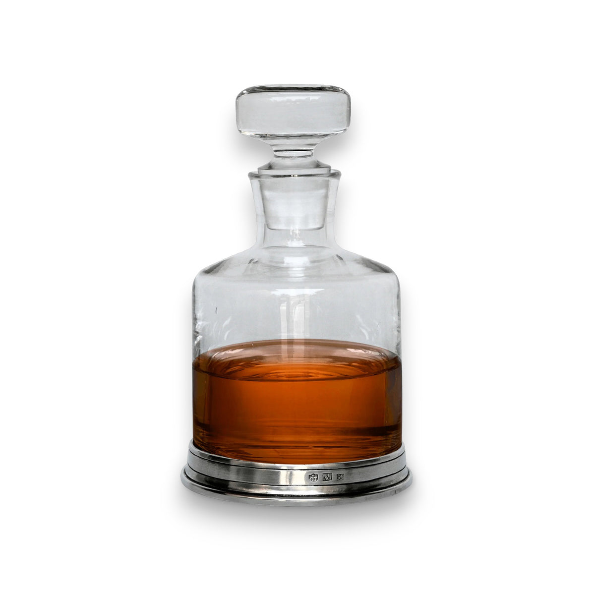 The MATCH - PEWTER BOTTOM SPIRITS DECANTER by MATCH, filled halfway with amber liquid, features clear lead-free crystal and a round stopper, resting on a reflective base against a white background.