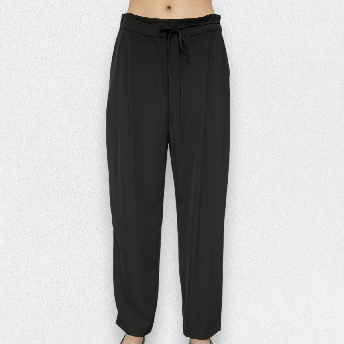 A person is wearing the MEIMEIJ - DRAWSTRING TROUSER PANT from the brand MEIMEIJ. These black, high-waisted trousers feature a loose fit and are made from a blend of polyester and elastane, complete with a tie belt. The image is taken from the waist down, showcasing the trousers in full against a plain white background, with the person&#39;s feet partially visible at the bottom.