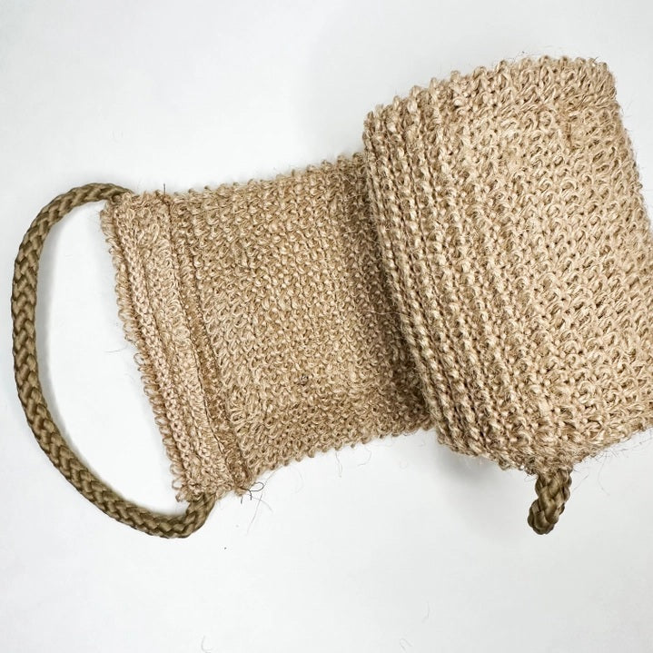 A close-up of the SMILE BOUTIQUES NATURAL ORGANIC JUTE BACK SCRUBBER, featuring a brown, woven jute design with a braided handle at one end and laid flat on a white background—this handmade bath accessory offers a sustainable upgrade to your shower routine.